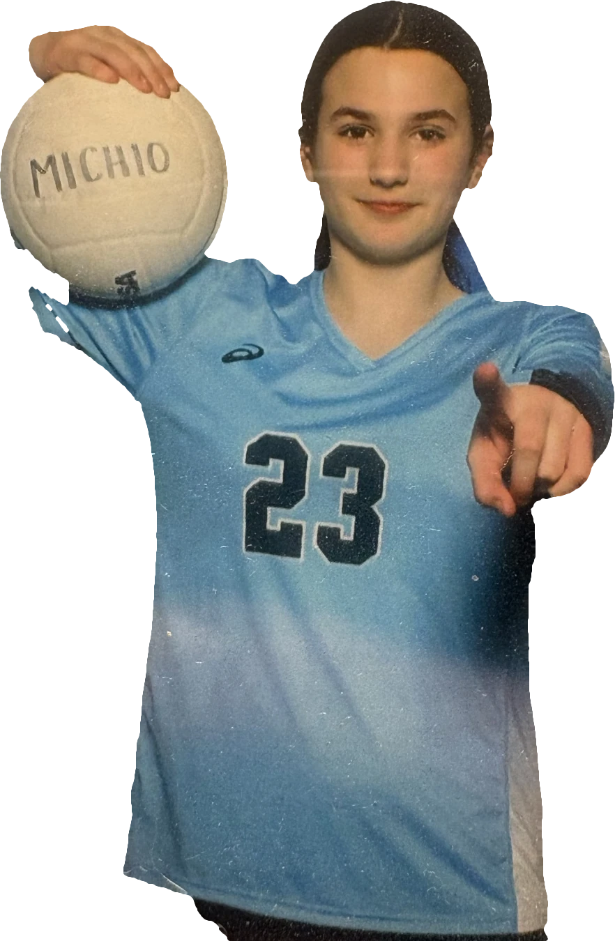 Adrianna Dingus in her light-blue Michio #23 jersey, holding a volleyball and pointing at the camera